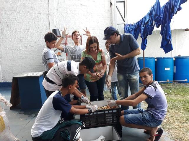 Alunos utilizando a compostagem e, ao fundo, coletores de água da chuva